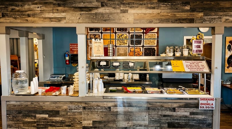 A self-serve buffet counter with various Indian dishes, snacks, and drinks in a restaurant.