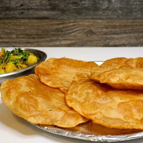 Golden fried puri bread on a foil plate with a side of potato curry.