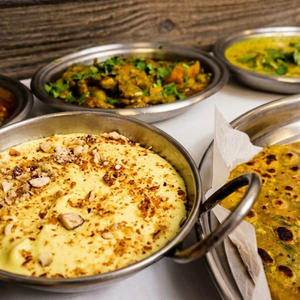 A spread of Indian dishes, including curries, a yellow dessert with nuts, and flatbread.