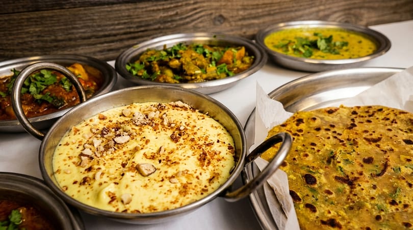 A spread of Indian dishes, including curries, a yellow dessert with nuts, and flatbread.